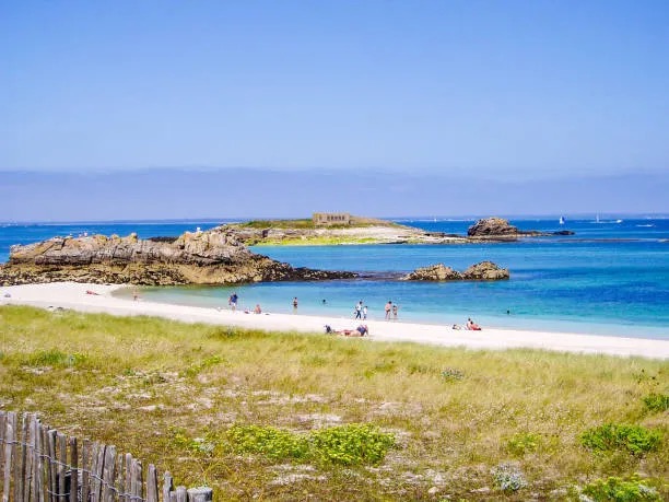 Plage de sable blanc et eaux turquoise du lagon des Glénan, avec un îlot rocheux en arrière-plan