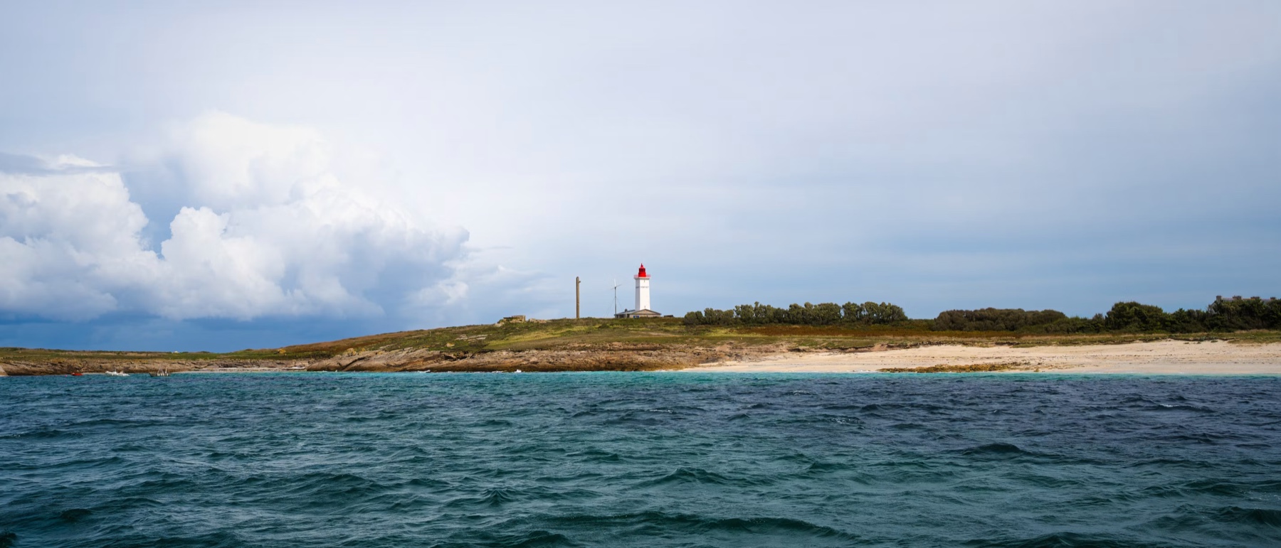 Le phare de Penfret et sa plage de sable blanc dans l'archipel des Glénan, vus depuis la mer