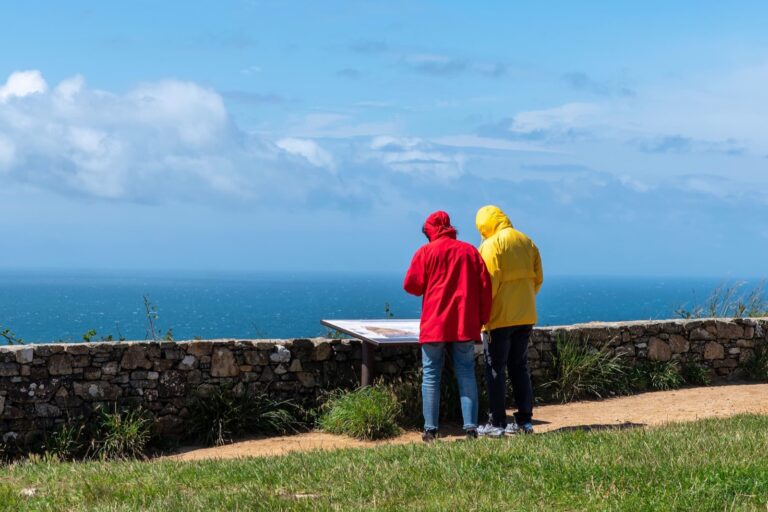 Deux promeneurs en imperméable devant une table d'orientation sur un sentier côtier de Bretagne, face à la mer